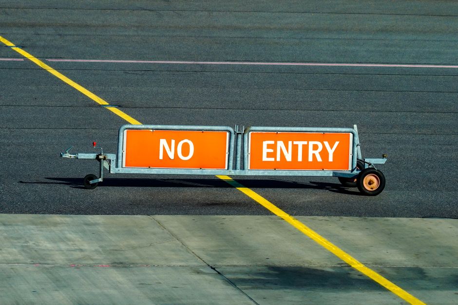 A warning sign indicating no entry on an airport taxiway with a bold yellow line.
